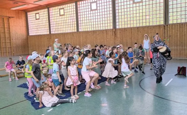 Kinder sitzen in der Turnhalle und schauen einer Theateraufführung zum Thema Verkehrssicherheit zu.