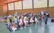 Kinder sitzen in der Turnhalle und schauen einer Theateraufführung zum Thema Verkehrssicherheit zu.