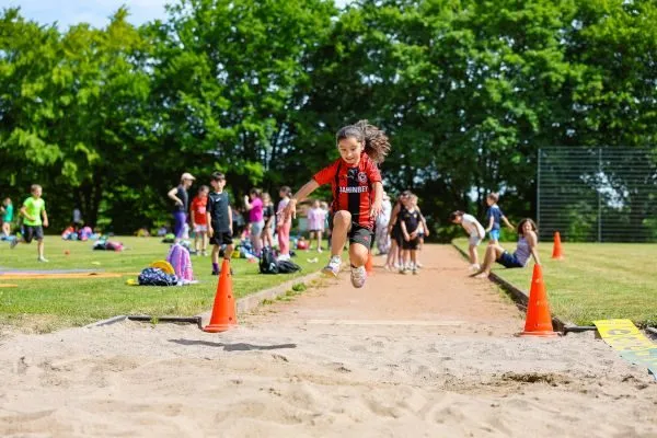 Kinder beim Weitsprung auf dem Sportplatz im Freien bei sommerlichem Wetter