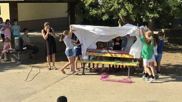 Bunt gestaltete Mitspielbank auf einem Grundschulhof, umgeben von Kindern bei der Einweihungsfeier